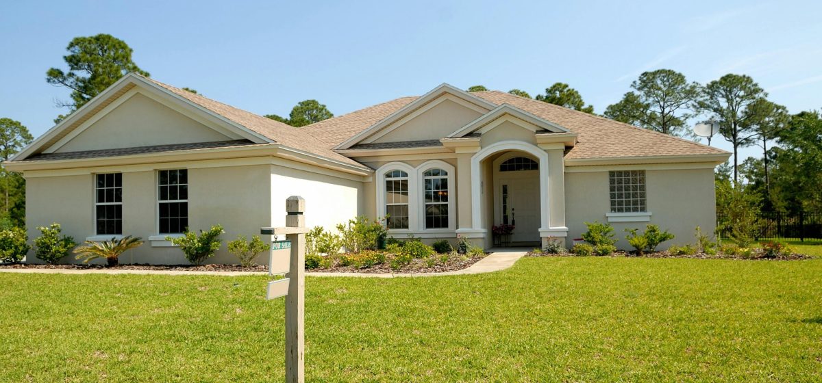 Beautiful suburban house with lush lawn, showcasing a for sale sign under a clear blue sky.